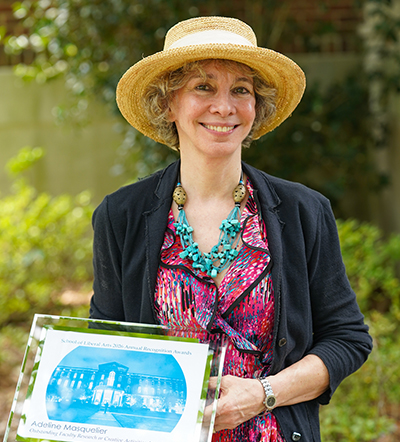 Smiling woman in a straw hat holding an award plaque with a blue building graphic.
