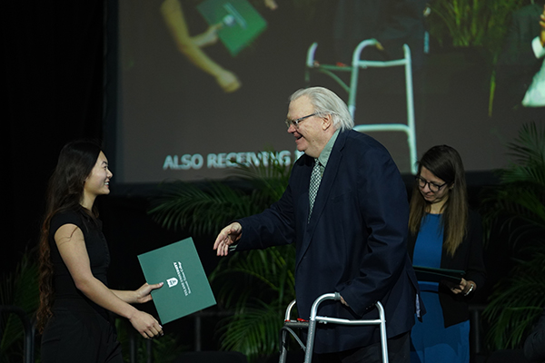 Woman receives green certificate from older man with walker at an awards ceremony.