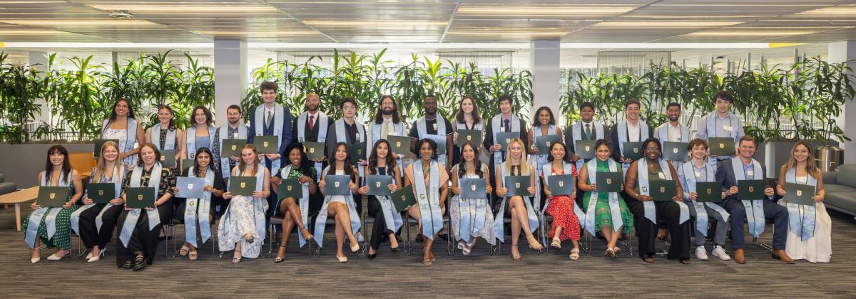 Smiling graduates in academic stoles hold certificates, posed in a modern indoor setting.