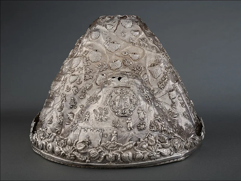 Ornate silver object decorated with raised figures, plants, buildings, and religious symbols, associ