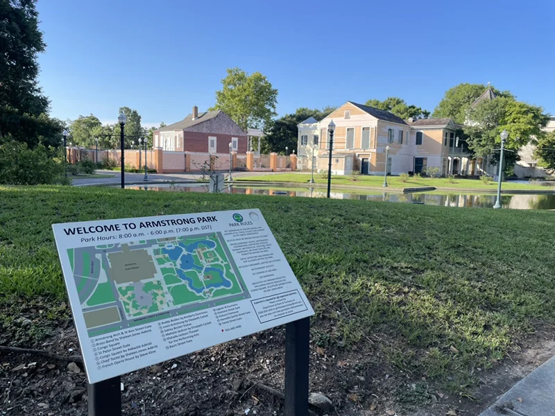 Informational map sign for Armstrong Park, with historic buildings and a pond in the background.