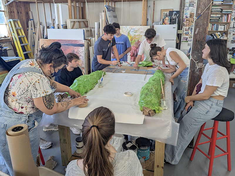 Group of young artists collaborating on a project with green forms on paper in an art studio.
