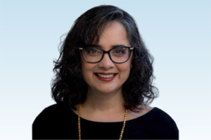 Smiling woman with dark curly hair and glasses, on a light blue background.