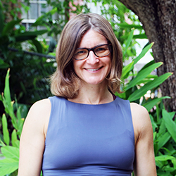 Professional portrait of woman with brown hair smiling against foliage backdrop.