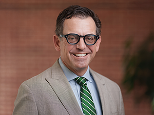 Smiling man in glasses, tan suit, and green striped tie.