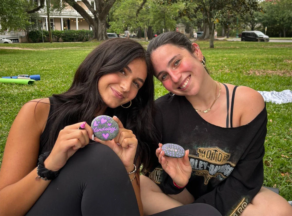 Two students displaying painted rocks at an outdoor gathering in Audubon Park