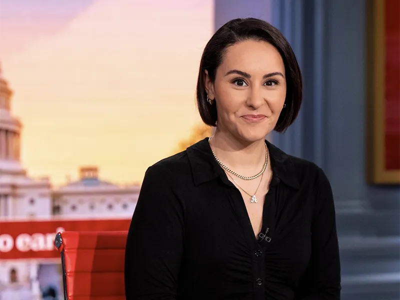 Ali Vitali smiles in a studio with a Capitol building background.
