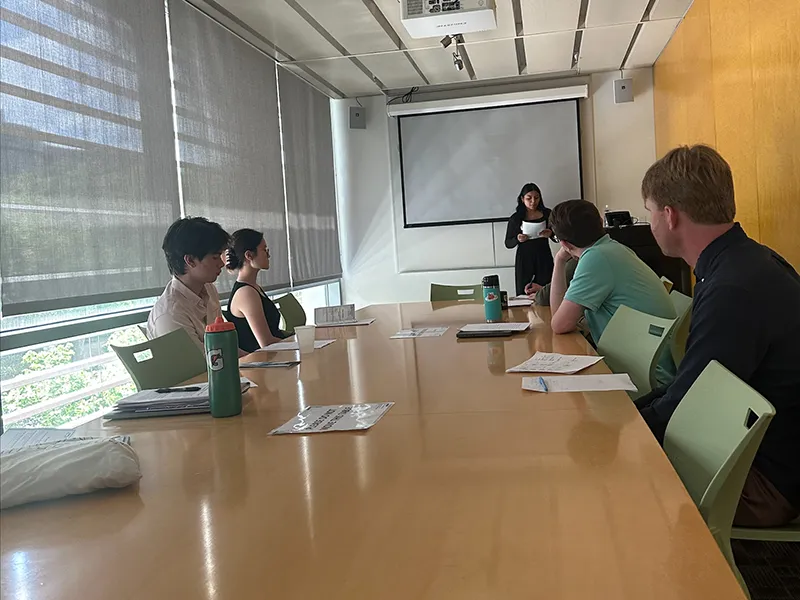Woman presenting to a small group in a conference room with a projector.