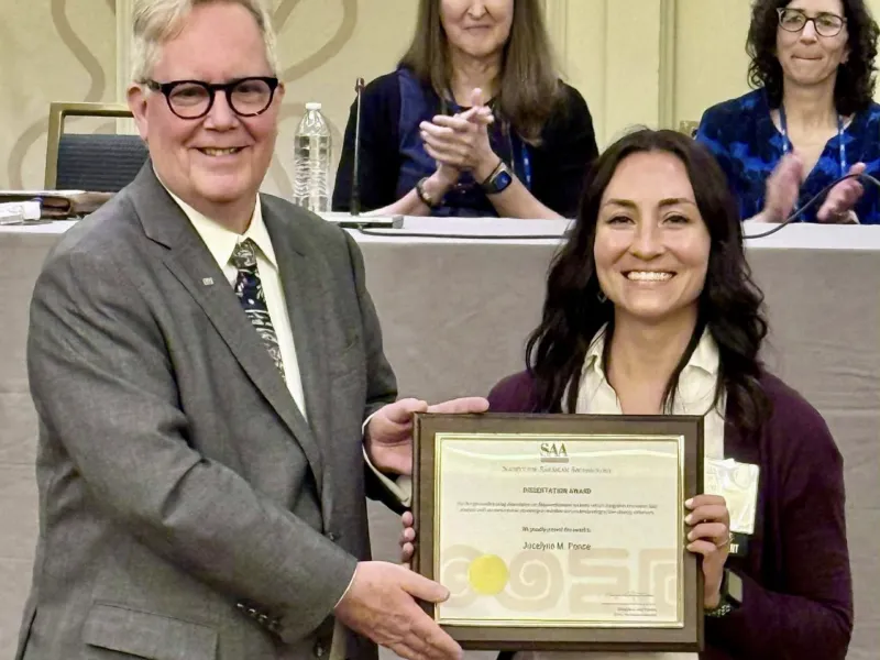 Man in suit presents framed certificate to a smiling woman on stage.
