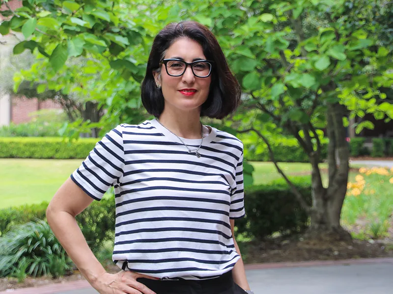 Woman with dark hair and glasses smiles in a striped shirt outdoors.