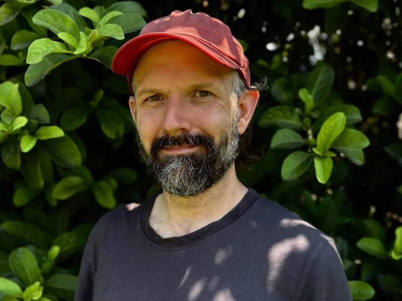 Anthony Baab smiling wearing a dark grey shirt and pink cap.