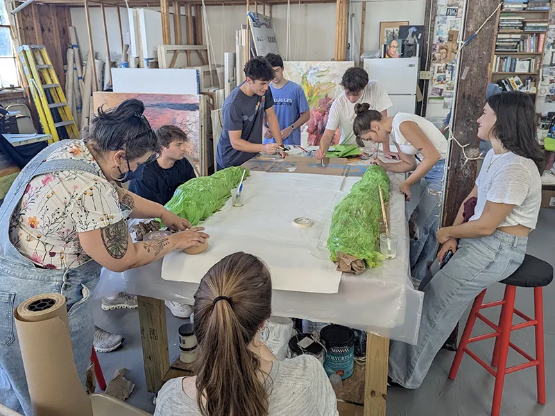 Group of young artists collaborating on a project with green forms on paper in an art studio.