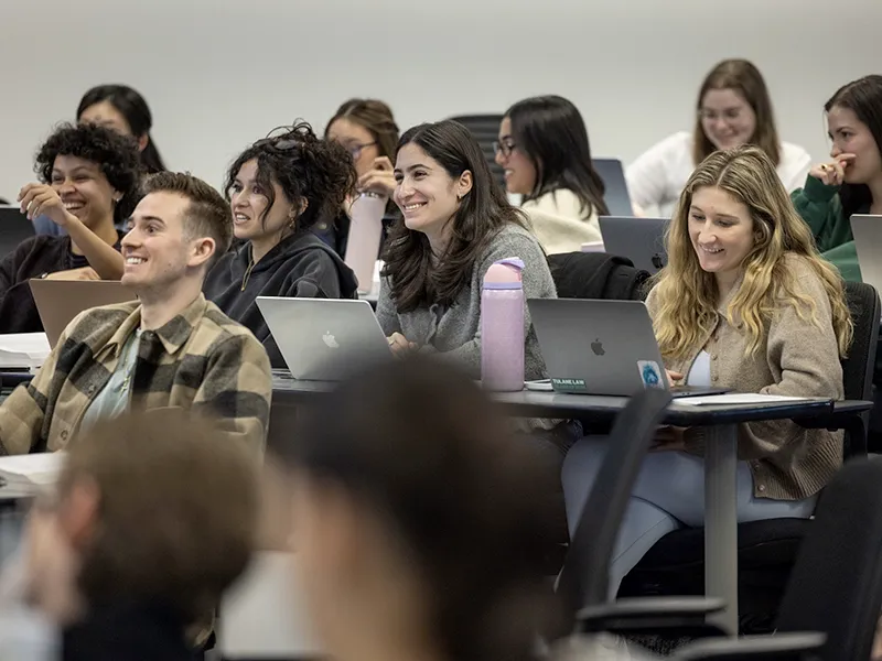 Students smiling and laughing in a classroom with laptops