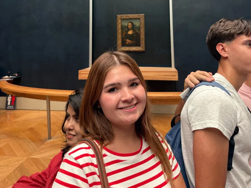 Sophie Slade smiles at camera in front of the Mona Lisa painting.